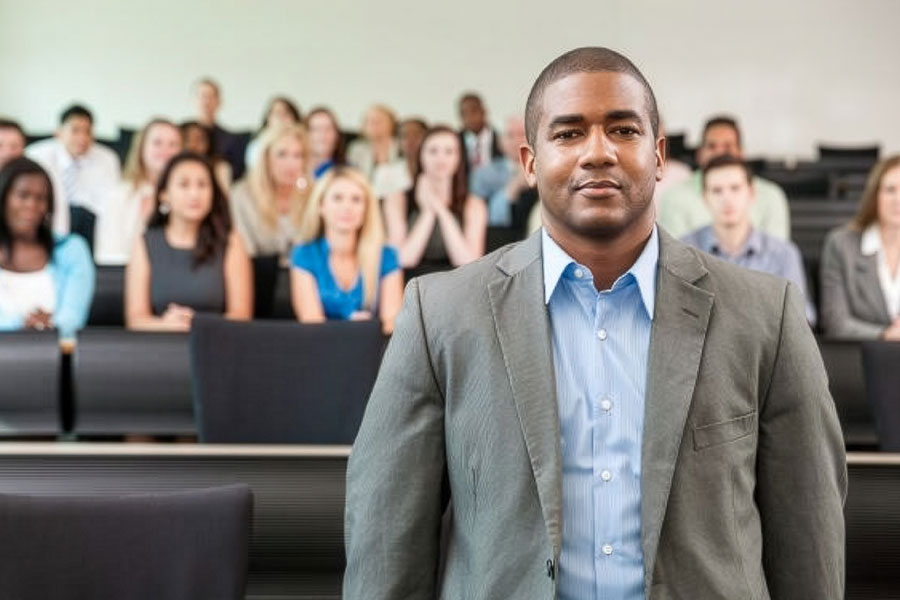 Person standing in a classroom with seated students in the background during a lecture.